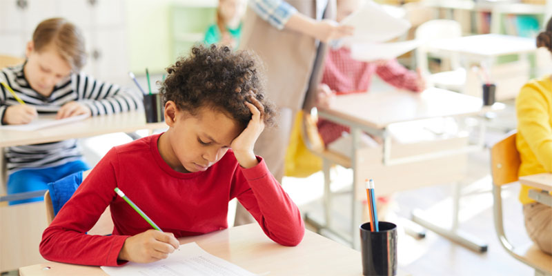 A child sitting in class at their desk and struggling with work