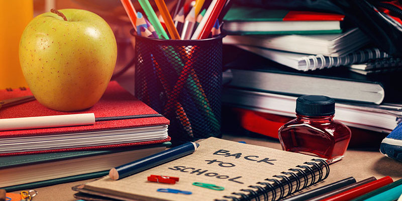 A desk covered in books and papers, school supplies, and an apple.