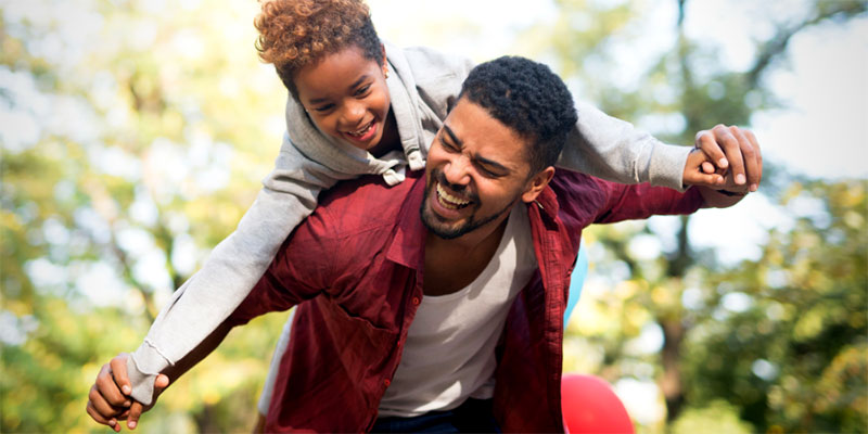 A father picks up his daughter while they both laugh and play in the park.