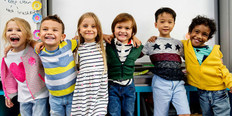 A group of kindergarteners smiling and posing for the camera with their arms around each other's shoulders.