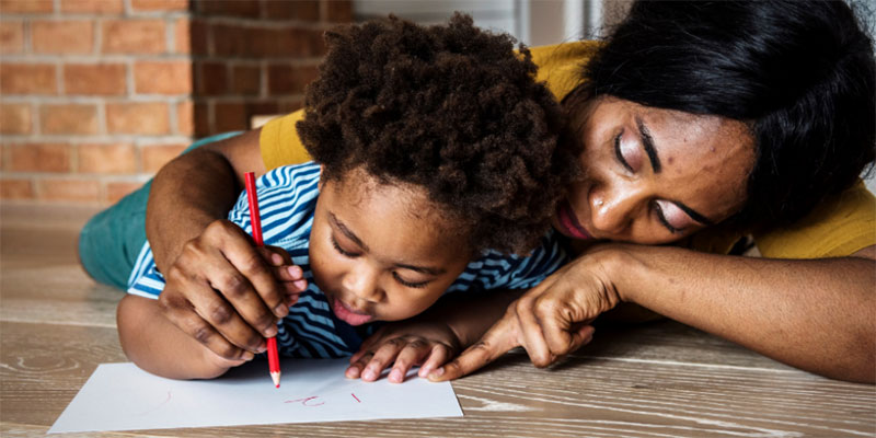 A mother holds a pencil with her child and teaches them to write.