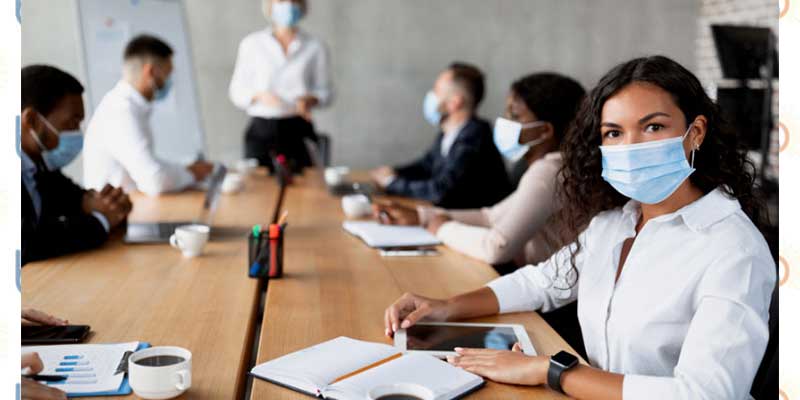 A woman sitting in a board room meeting with all participants masked